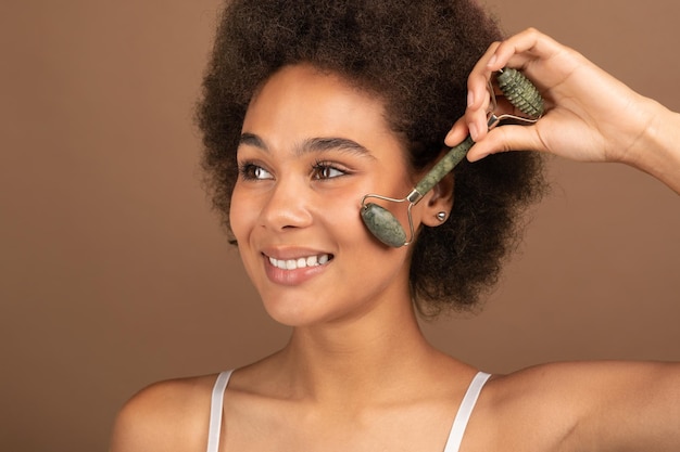 Photo heureuse jolie jeune femme bouclée noire avec une peau parfaite applique de la poudre ou du fard à joues avec un pinceau sur le visage