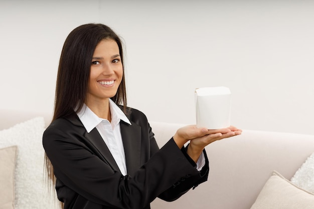 Heureuse jolie jeune femme étend ses mains pour recevoir une boîte en papier avec de la nourriture Restauration rapide pendant la pause déjeuner au bureau Livraison de restauration rapide