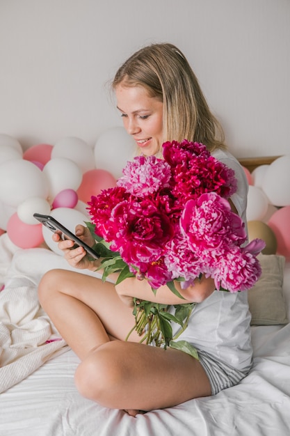 heureuse jolie jeune femme à la maison dans la chambre au lit tenant des fleurs prendre un selfie par téléphone portable