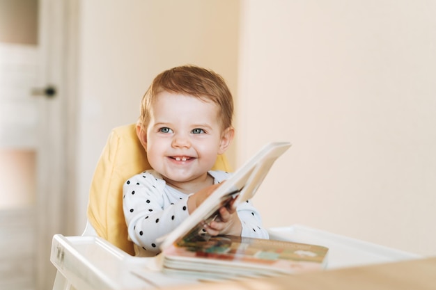 Heureuse jolie petite fille dans un siège d'appoint lisant un livre pour enfants à la maison