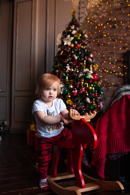 Heureuse jolie petite fille est assise sur un chevreuil en bois vintage avec décoration de Noël