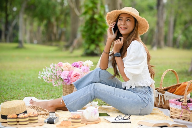 Heureuse et joyeuse jeune femme asiatique parlant au téléphone pendant un pique-nique dans le jardin verdoyant