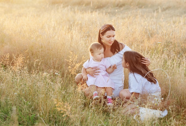 Heureuse maman avec deux petites filles sur le terrain d'été au coucher du soleil