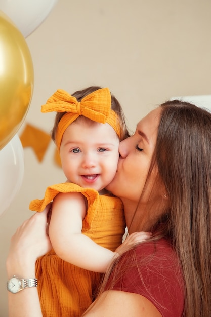 Heureuse maman embrasse sa fille d'un an en vêtements jaunes, photo en studio pour un an de l'enfant