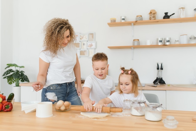 Heureuse maman et enfants mélangeant les ingrédients pour la pâte à gâteau, à tarte ou à biscuits maison dans la cuisine.