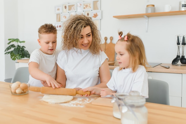 Heureuse maman et enfants mélangeant les ingrédients pour la pâte à gâteau, à tarte ou à biscuits maison dans la cuisine.