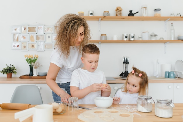 Heureuse maman et enfants mélangeant les ingrédients pour la pâte à gâteau, à tarte ou à biscuits maison dans la cuisine.