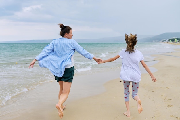 Heureuse maman et fille courant sur la plage de la mer tenant la main vue arrière