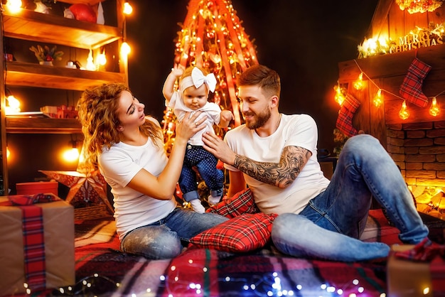 Heureuse maman et papa jouant avec sa petite fille assis près du sapin de Noël et de la cheminée