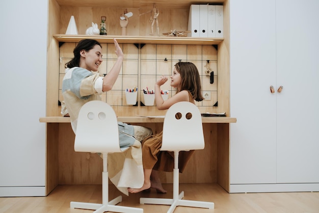 Heureuse maman et petite fille mignonne se donnant un high five à faire leurs devoirs