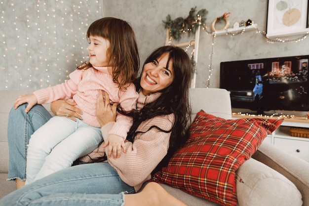 Heureuse maman et sa fille sautant ensemble sur le canapé, main dans la main, mère jouant avec une jolie petite fille à la maison, jeune maman et bébé adorent passer du temps ensemble.