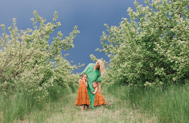 Une heureuse maman vêtue d'une robe verte se promène avec ses deux petites filles dans le jardin avant la pluie. bonheur familial et soins maternels