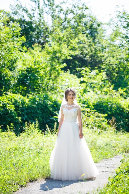 Heureuse mariée dans une longue robe de mariée blanche et voile dans un parc verdoyant sur la nature. Image de mariage d'une jeune fille, maquillage et coiffure pour femmes. Notion de mariage