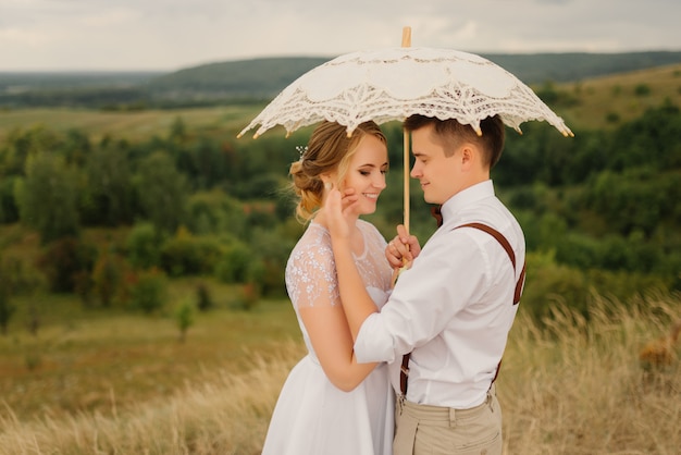 Heureuse mariée et le marié s'embrassent et tiennent un parapluie vintage sur la nature. Mariage, concept d'amour.