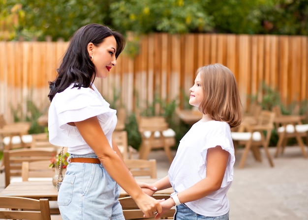 Heureuse mère et adolescente debout à l'extérieur sur la terrasse du café et se tiennent la main. Notion de famille