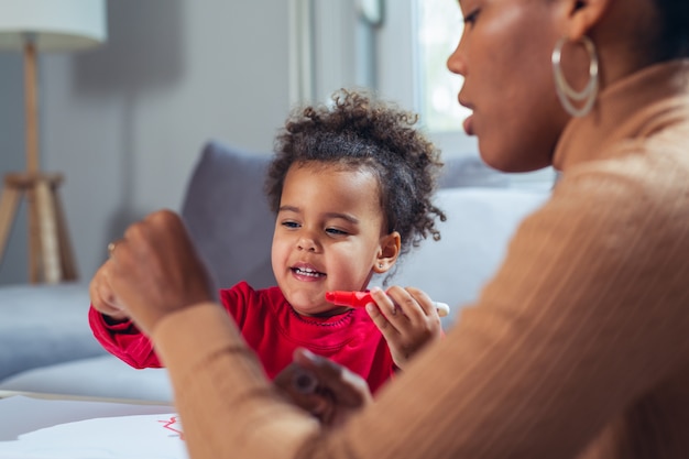 Heureuse mère afro-américaine aidant sa fille à colorier