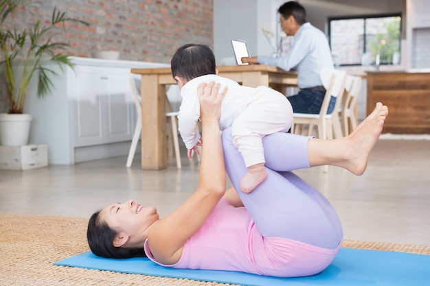 Heureuse mère et bébé fille exerçant sur un tapis à la maison