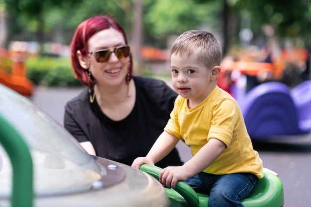 Photo heureuse mère divertissant son petit fils atteint du syndrome de down sur une aire de jeux en ville