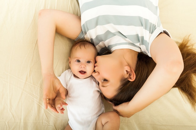 Heureuse mère embrassant un bébé allongé sur un lit