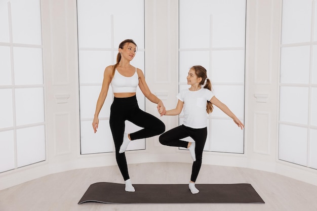 heureuse mère et enfant fille faisant du yoga debout sur le sol dans la salle de sport