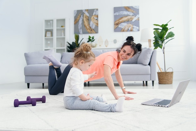 Heureuse mère faisant des exercices du matin dans la pose de yoga pendant que sa petite fille joue à la maison. Jeune maman adorable s'amusant à pratiquer la méditation relaxante le week-end sans stress avec bébé.