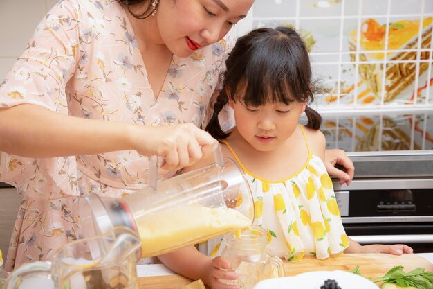 Heureuse mère de famille asiatique et sa fille aiment préparer des fruits fraîchement pressés avec des légumes pour faire des smoothies pour le petit déjeuner ensemble dans la cuisine. concept de régime et de santé.