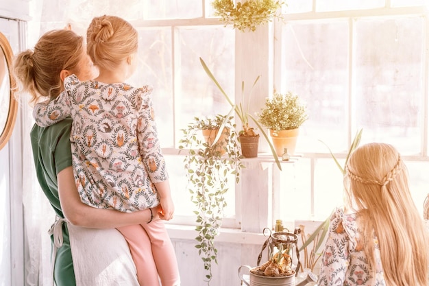 Heureuse mère de famille avec enfants filles filles s'amuser dans la vie de famille à la campagne de banlieue le jour de printemps ensoleillé maman et enfants candides debout près de la fenêtre avec des gens de plantes amour et soin moment flare