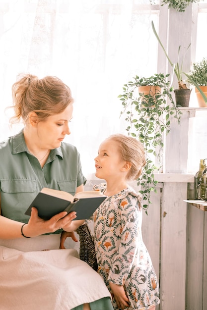 Heureuse mère de famille avec une jolie petite fille fille s'amuser ensemble dans la maison de campagne de la banlieue le jour d'été ensoleillé maman candide étreignant et lit un livre aux enfants que les gens aiment et soignent