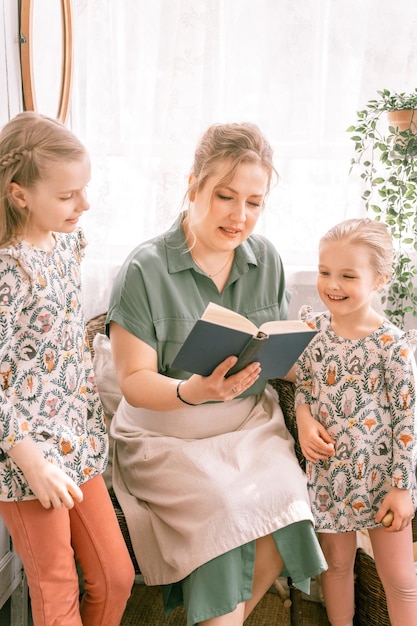 Heureuse mère de famille avec de mignons petits enfants filles filles s'amusent ensemble dans la maison de campagne de banlieue le jour d'été ensoleillé maman candide étreignant et lit un livre aux enfants que les gens aiment et soignent