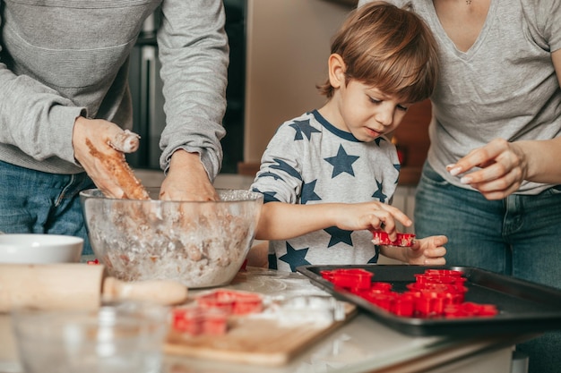 Heureuse mère de famille, père et fils préparant des biscuits de Noël dans une cuisine confortable à la maison, mélangeant de la pâte, Petit garçon aide maman et papa à faire des biscuits.