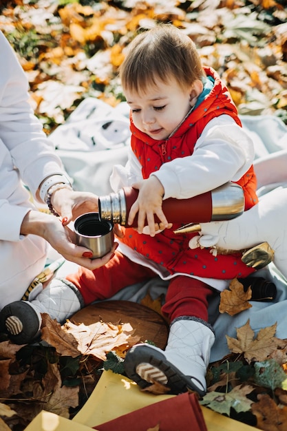 Heureuse mère de famille et petite fille en bas âge ayant un pique-nique d'automne avec thermos rouge et tasse