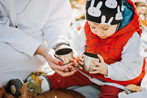 Heureuse mère de famille et petite fille en bas âge ayant un pique-nique d'automne avec thermos rouge et tasse