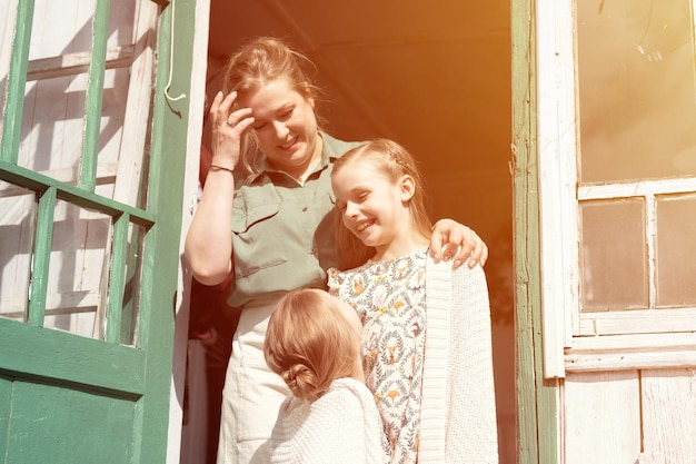 Heureuse mère de famille avec de petits enfants, les filles aident à s'amuser dans la vie de campagne de la banlieue le jour de la lessive, une maman candide embrasse et couvre les enfants avec un plaid et fait des corvées sur le porche de la maison de campagne