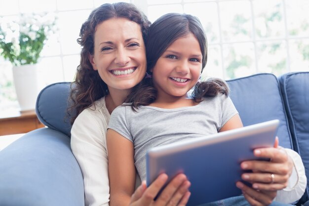 Heureuse mère et fille assise sur le canapé et à l&#39;aide de tablette