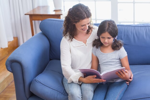 Heureuse mère et fille assise sur le canapé et livre de lecture
