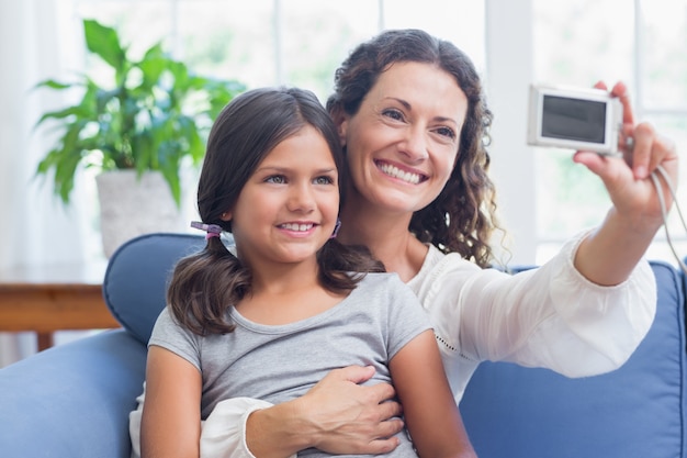 Heureuse mère et fille assise sur le canapé et prenant selfie