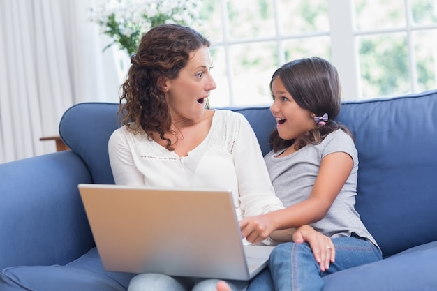 Heureuse mère et fille assise sur le canapé et utilisant un ordinateur portable