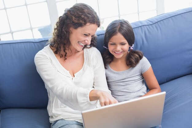 Heureuse mère et fille assise sur le canapé et utilisant un ordinateur portable