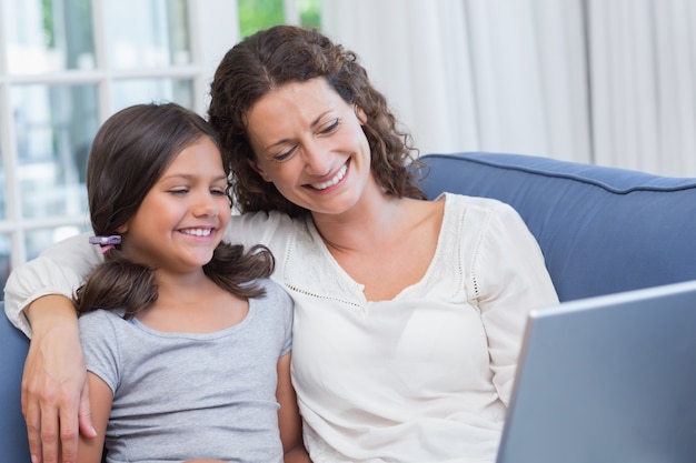 Heureuse mère et fille assise sur le canapé et utilisant un ordinateur portable