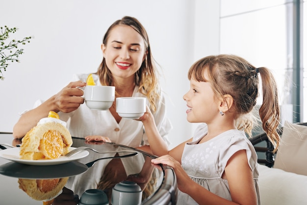 Heureuse mère et fille de boire du thé et de manger un délicieux gâteau avec une garniture à l'orange et de la crème fouettée