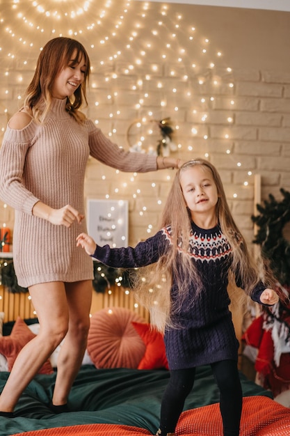 Heureuse mère et fille dansant sur le lit, attendant Noël, joyeuses fêtes, belle décoration sur fond