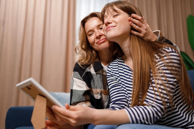 Heureuse mère et fille étreignant assis sur un canapé et regardant une photo encadrée