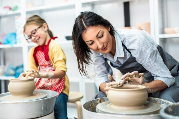 Heureuse mère et fille faisant de la poterie en argile sur une roue tournante.