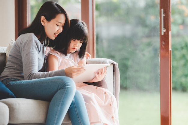 Heureuse mère et fille de famille asiatique utilisant une tablette numérique pour étudier ensemble à la maison