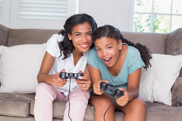 Heureuse mère et fille jouant à des jeux vidéo ensemble sur le canapé