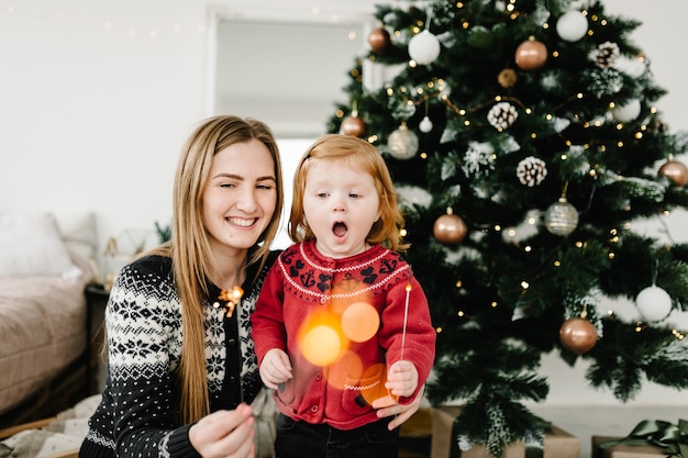 Heureuse mère et fille s'amusant avec des cierges magiques célébrant Noël à la maison