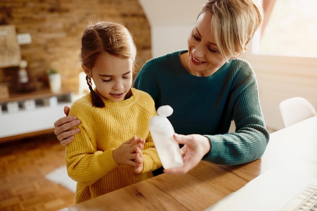 Heureuse mère et fille utilisant un désinfectant pour les mains à la maison