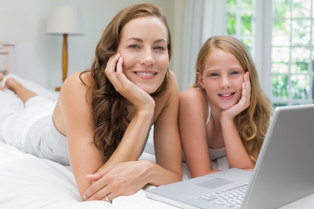 Heureuse mère et fille utilisant un ordinateur portable dans la chambre