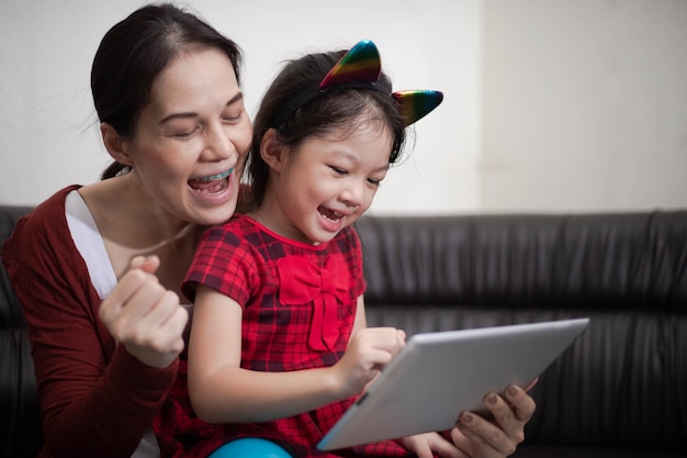Heureuse mère et fille utilisant une tablette numérique assise sur un canapé pour étudier en ligne à la maison