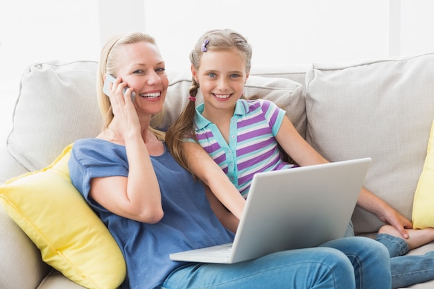 Heureuse mère et fille utilisant des technologies sur le canapé